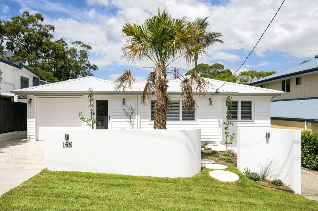 Modern white house with a flat roof, centred palm tree, and a green lawn.