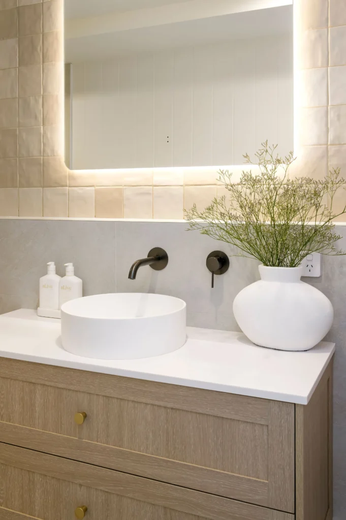 Modern bathroom with a vessel sink on a wooden vanity, backlit mirror, and minimalist decor.