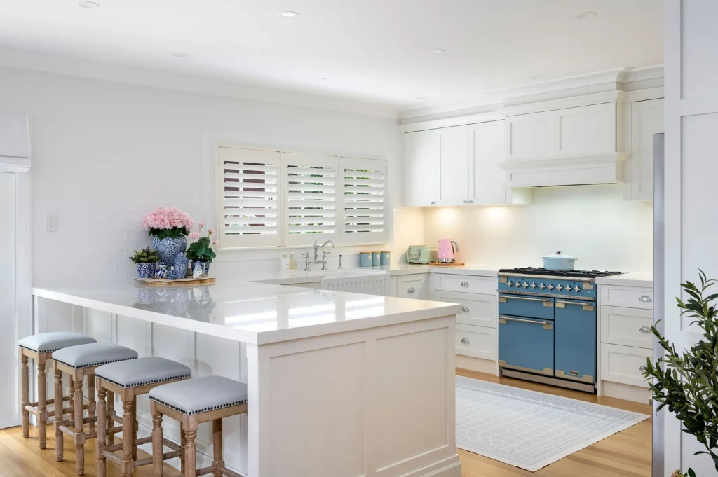 Bright kitchen with a large white island, wooden stools, and a blue vintage-style stove.