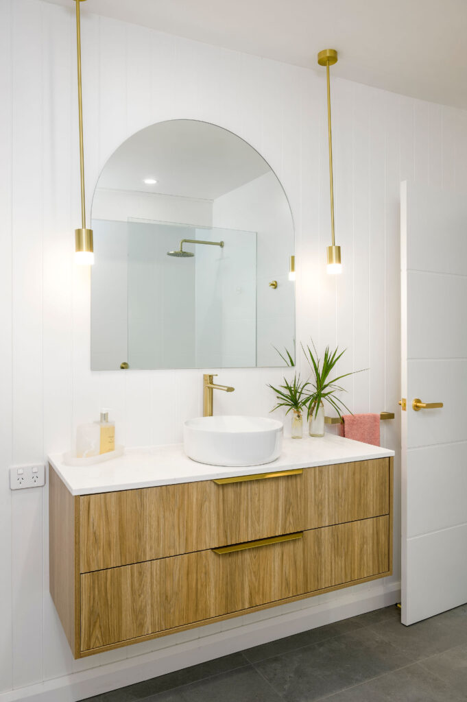 Bathroom renovation featuring timber vanity with white stone countertop and gold pendant lights